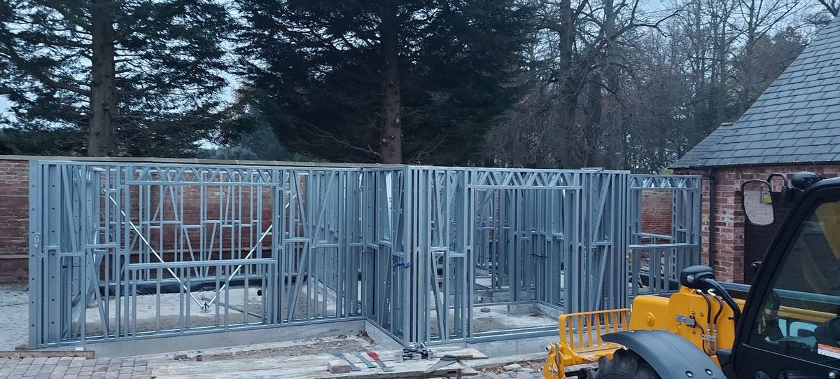 Steel frames being erected on a cloudy day, with a telehandler on site