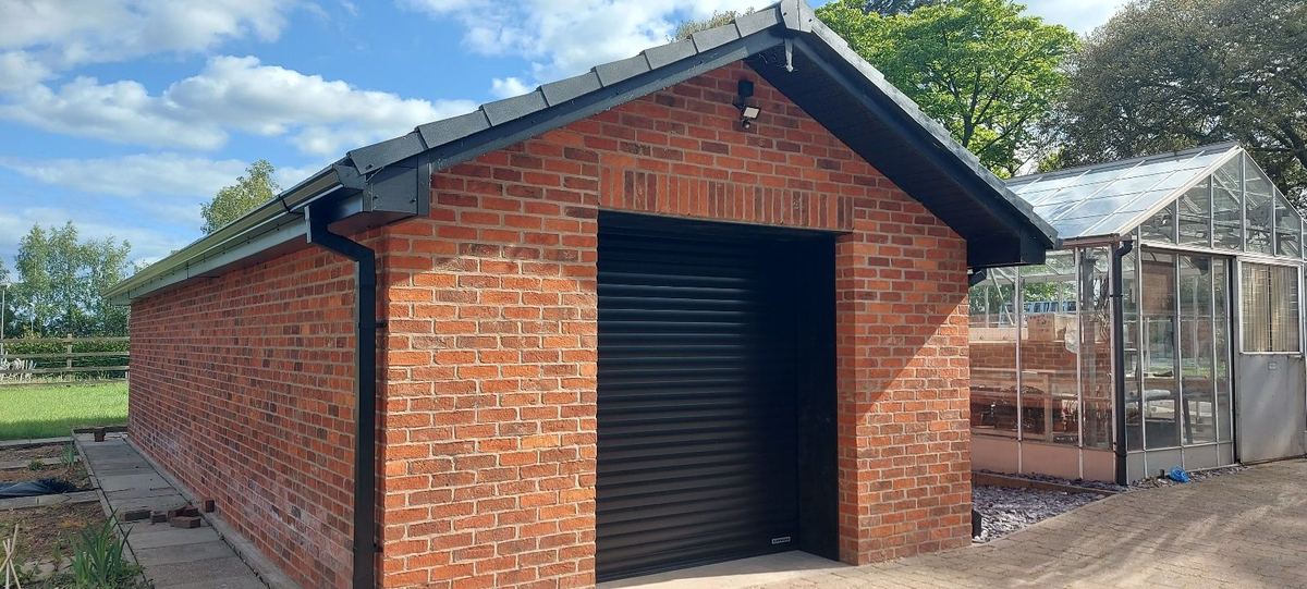 The completed brick store with a roller door, beside the replacement greenhouse